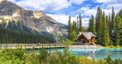 Wooden lodge sitting on the shore of a turquoise lake reflecting in the calm water with tourists