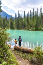 Tourists standing on a log are enjoying the breathtaking view of the turquoise water of emerald