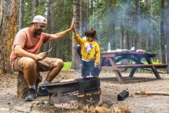 Father and son are giving a high five while grilling food over a campfire, enjoying quality time