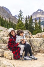 Mother and son sitting on rocks, soaking in the stunning views of turquoise peyto lake and