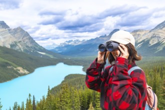 Female hiker using binoculars, admiring the scenic turquoise waters of peyto lake and the majestic
