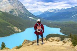 Female hiker standing on a cliff, soaking in the stunning panoramic view of turquoise peyto lake