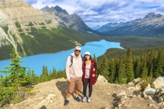 Two hikers are standing on a mountaintop, enjoying the breathtaking panoramic view of the turquoise