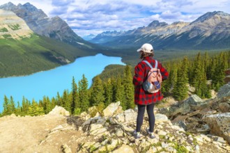 Female hiker wearing a backpack, standing on a rocky viewpoint and admiring the stunning turquoise