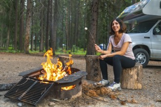 Female tourist roasting marshmallows over a campfire in a campground in banff national park, next