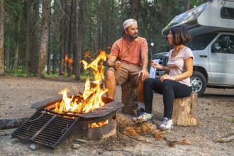 Tourists roasting marshmallows over campfire near their campervan, enjoying a peaceful evening in