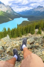 Hiker resting on a rocky mountain top, soaking in the stunning panoramic view of turquoise peyto