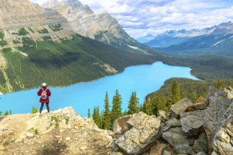 Hiker standing on a rocky cliff, overlooking the turquoise waters of peyto lake, surrounded by