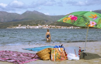 Sunshade and swimwear blurred on the beach or Plage de la Roya, in the back Saint-Florent on the