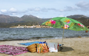 Sunshade and swimwear on the beach or Plage de la Roya, in the back Saint-Florent on the Gulf of