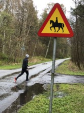 Person jogging on wet forest road with road sign for riding on horse in Ystad, Skåne County,