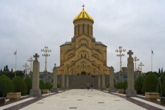 Grand cathedral with golden roof and stylish stone pillars against cloudy sky, Sameba Cathedral,