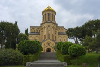 A magnificent church with a golden dome and symmetrical steps surrounded by lush greenery, Sameba