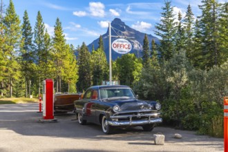 Vintage car towing a wooden boat trailer parked near a vintage gas pump by the johnston canyon