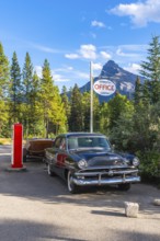 Classic car with a wooden boat parked in front of the johnston canyon office sign, with castle