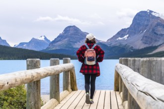 Female tourist with backpack walking on wooden bridge enjoying turquoise color water of bow lake
