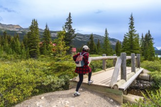 Female tourist walking across a wooden bridge at bow lake, framed by a red roofed building,