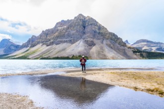 Female hiker stands at the edge of bow lake, admiring the turquoise water and imposing mountain