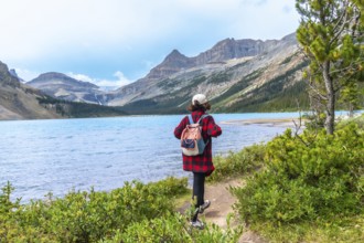 Female tourist with backpack walking along hiking trail by turquoise bow lake with crowfoot glacier