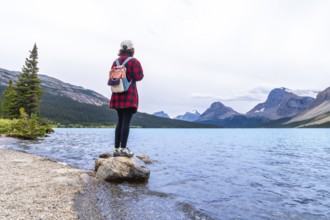 Female tourist standing on a rock at bow lake, admiring the turquoise waters and majestic mountains