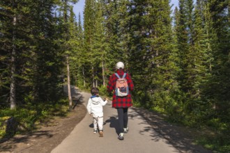 Mother and child holding hands, enjoying a leisurely hike along a paved path, surrounded by the