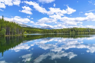 Calm waters reflecting a stunning cloudy sky over herbert lake, surrounded by lush pine forests and