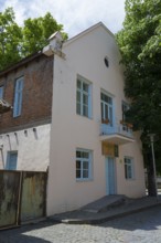 Two-storey building with bricks and blue door, surrounded by trees on a sunny day, Katharinenfeld