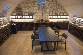 Wine cellar with long tasting table and chairs, surrounded by illuminated wine racks on stone