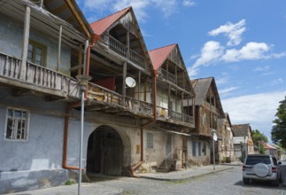 Street view with old wooden houses and balconies under blue sky with parked cars, traditional