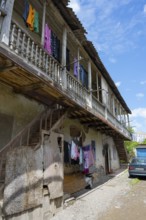 An old building with wooden balcony and clotheslines, next to it is an old car under a blue sky,