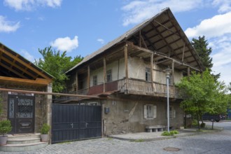 Old, two-story building with wooden roof and balconies surrounded by trees, traditional German