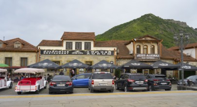 Street scene with cars parked in front of a restaurant with mountain backdrop in the background,