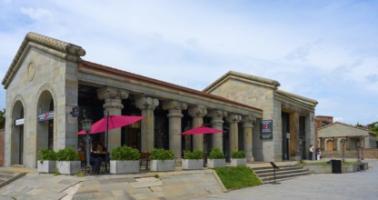 Historic stone building with ancient columns and red umbrellas under cloudy sky, Mtskheta,