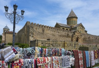 Rugs in front of a historic wall with a cathedral in the background under a blue sky,
