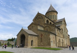 Impressive medieval stone cathedral with visitors under cloudy sky, Svetitskhoveli Cathedral,