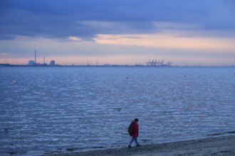 Person on the beach with a view of the sea and industrial areas in Wilhelmshafen right Jade-Weser