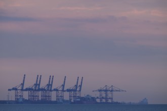 Cranes container bridges at Jade.Weser Port against a purple evening sky, calming atmosphere,