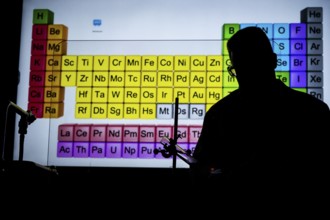 Silhouette of a chemistry teacher in front of an illuminated projection of the periodic table in
