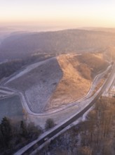 Aerial view of a hill in morning light with snow-covered roads and surrounding forest, future PV