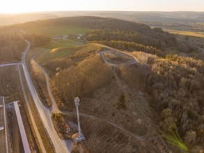 Hilly landscape with forest and roads in the warm light of sunset, future PV building on old