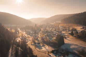 Aerial view of a village surrounded by snow-covered forests and mountains in the evening sun,