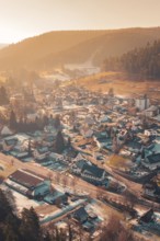 View of a snowy village in a wide valley at sunset, surrounded by wooded hills, Enzklösterle, Calw