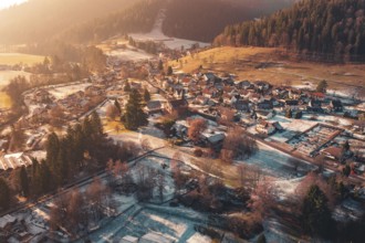 Expansive view of a village with snow-covered roofs surrounded by hills and forests, Enzklösterle,