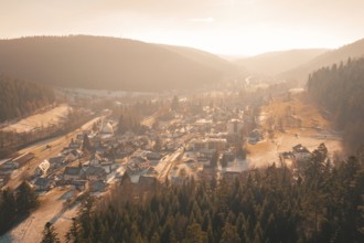 Panoramic view of a village with snow-covered roofs surrounded by forests and hills in the evening
