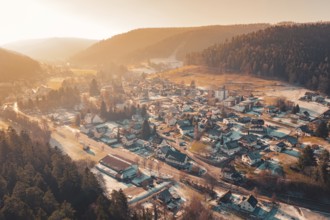 Extensive aerial view of a valley with snowy houses surrounded by mountains and warm sunset light,