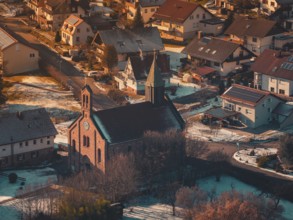Snowy village with church in the center, illuminated by warm sunset light and surrounded by