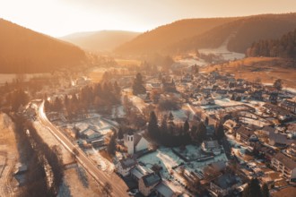 Snowy village from above, surrounded by mountains and illuminated by the warm atmosphere of sunset,