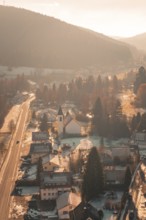 View of a village road with snowy houses and a church in the evening light, Enzklösterle, Calw