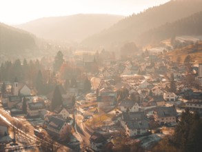 A picturesque village is situated in a valley surrounded by hilly forests and gentle autumn fog,