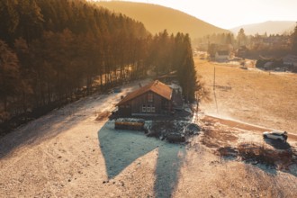 Wooden house surrounded by snow, nestled between meadow and forest in warm sunset light,